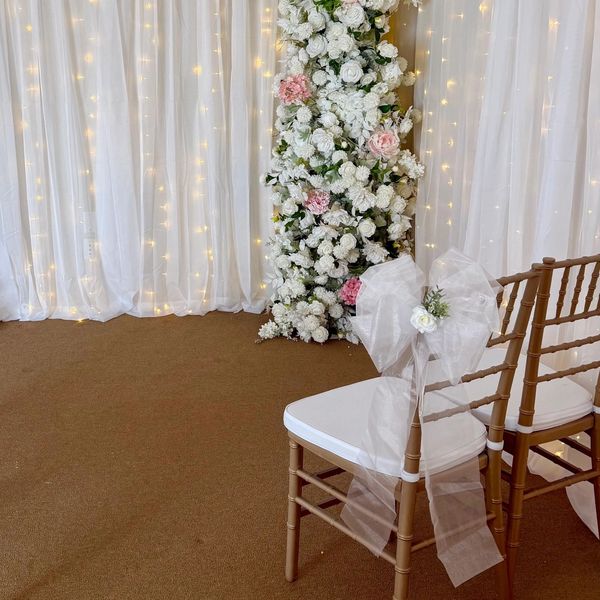 Elegant wedding setup with floral backdrop and decorated chairs.