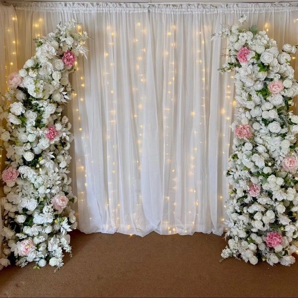 Elegant floral archway with white and pink flowers and twinkling fairy lights on white curtains.