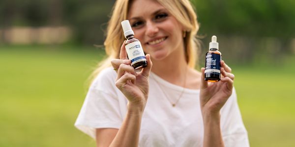 Woman holding two bottles of health supplements outdoors.