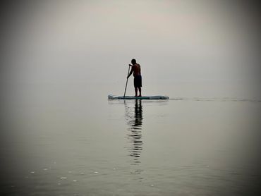 Person paddleboarding on calm, misty water with clear reflection.