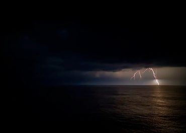 Lightning strikes over the ocean under a dark stormy sky at night.