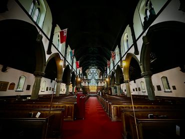 Interior of a traditional church with wooden pews and flags hanging from arches.