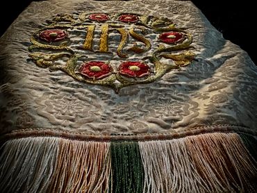 Ornate embroidered cloth with floral designs and gold letters IHS.
