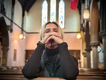 A woman in deep prayer inside a church with stained glass windows.