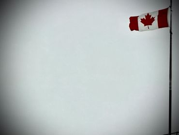 Tattered Canadian flag waving on a pole against a gray sky.