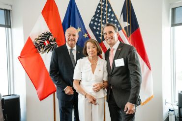 Three people posing with flags in the background.