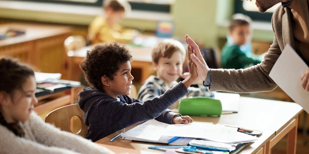 Teacher giving a high five to a student in classroom.