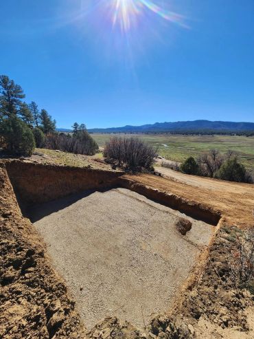 Excavated rectangular pit in a sunny rural landscape with clear blue sky.