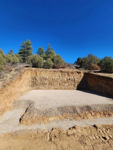 Excavated dirt area with a gravel base under a clear blue sky.