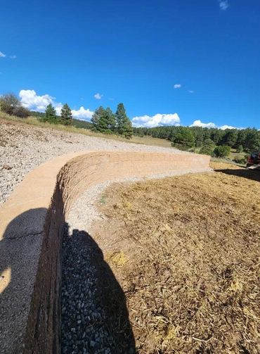 Curved retaining wall in a rural landscape under a clear blue sky.