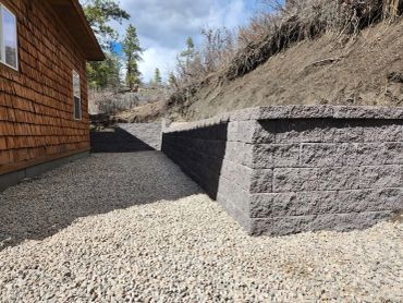Gravel pathway beside a house with a tall stone retaining wall.