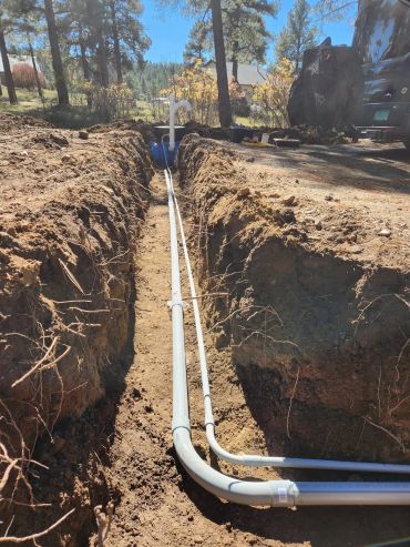 Two white PVC pipes laid in a trench outdoors during a sunny day.