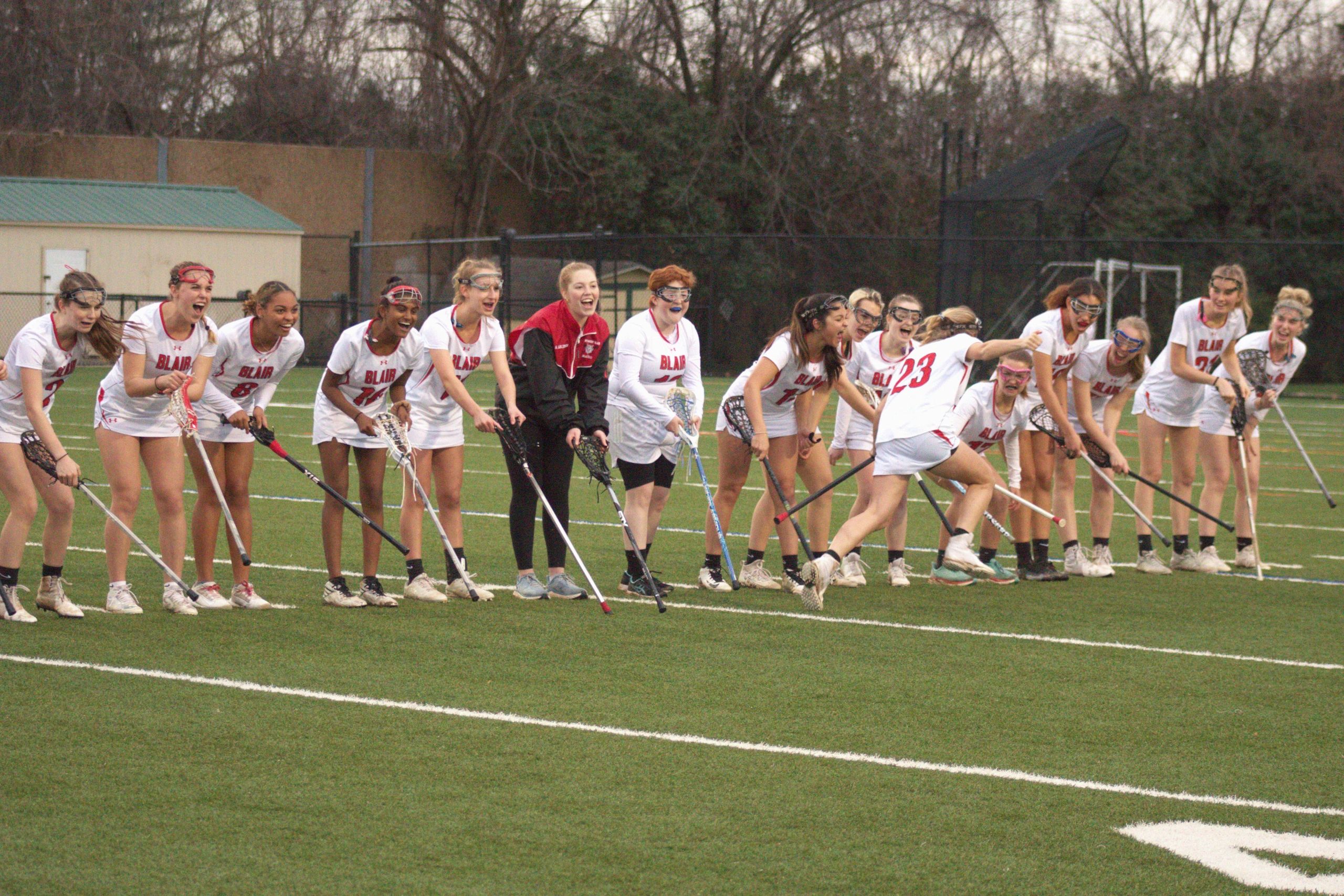 Girls' lacrosse team cheering on a player running by.