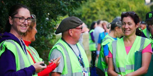 Volunteers in green safety vests chat outdoors in a group setting.