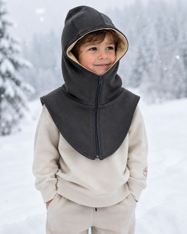 Smiling boy dressed warmly in winterwear with hood and jacket in snowy outdoors.
