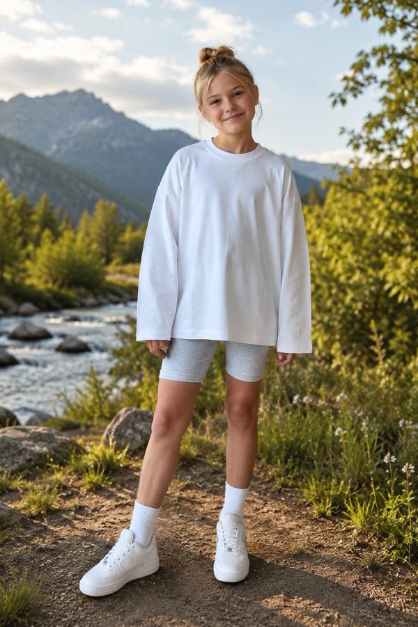 Smiling girl in white sweatshirt outdoors by a stream.