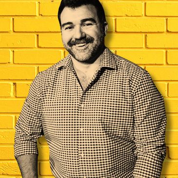 Smiling man in checkered shirt against yellow brick wall.