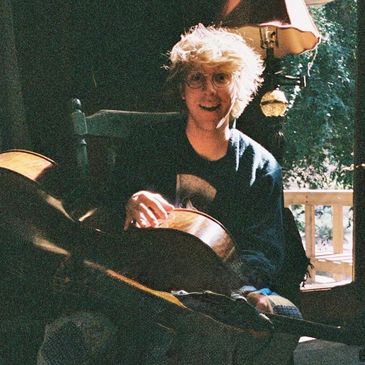 Person playing guitar in a cozy, sunlit room.