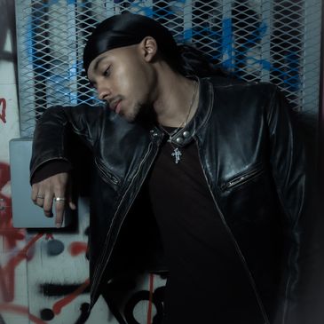 Young man in leather jacket leaning against a graffiti-covered wall.