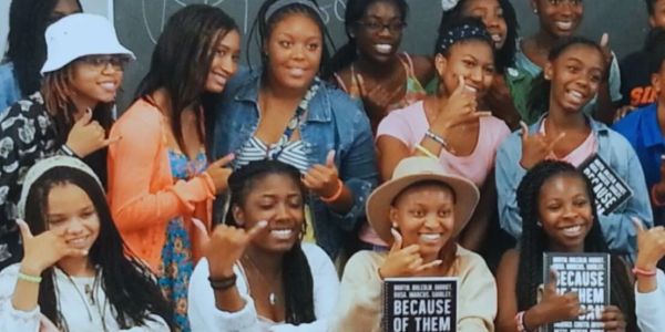 Group of smiling young women posing with thumbs-up and holding books.