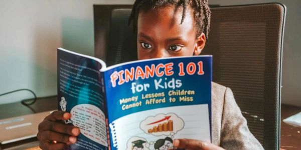 Child reading a book titled 'Finance 101 for Kids' about money lessons for children.