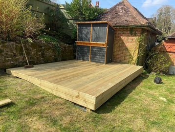 A newly built wooden deck in a garden with a broom leaning against a stone wall.