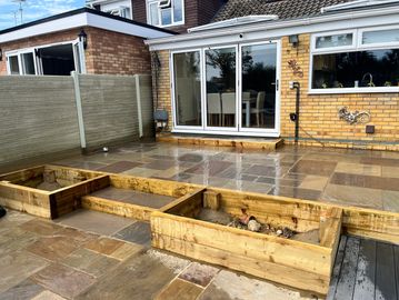 Newly tiled patio with wooden garden beds beside a house.