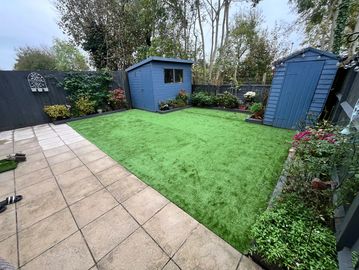 Neatly maintained backyard with green artificial grass and blue garden sheds.
