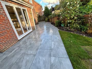 Newly tiled patio next to a garden with greenery and a house with glass doors.