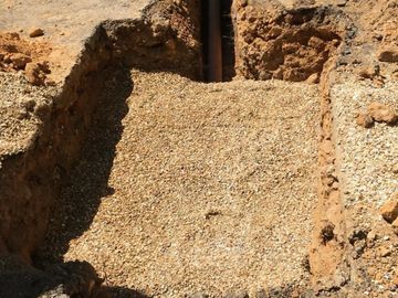 Trench with gravel and a visible pipe underground.
