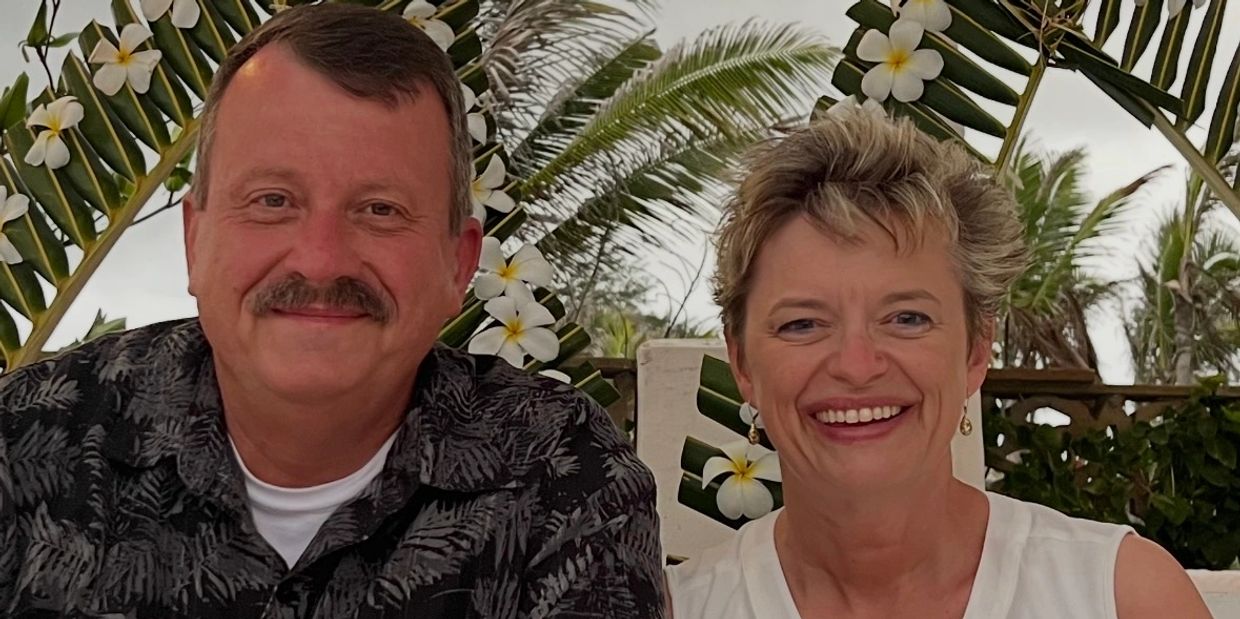 Smiling couple with tropical greenery and white flowers in the background.