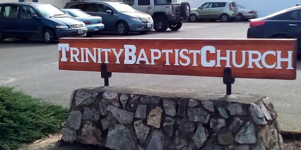 Sign for Trinity Baptist Church on a stone base in a parking lot.