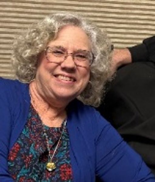 Smiling elderly woman with curly gray hair and glasses.