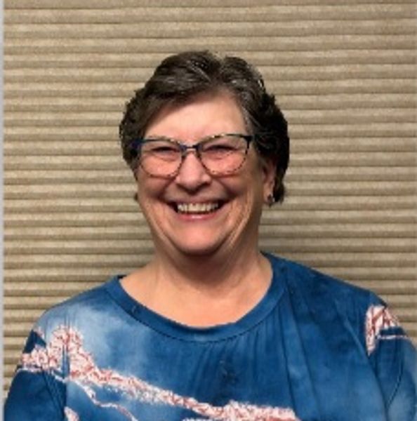 Smiling elderly woman wearing glasses and a blue shirt.
