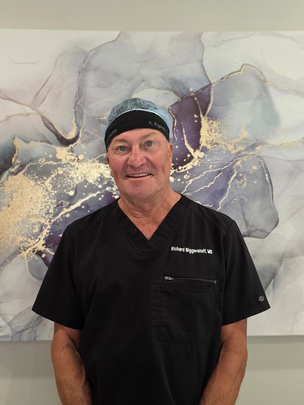 Smiling doctor in black scrubs and cap.