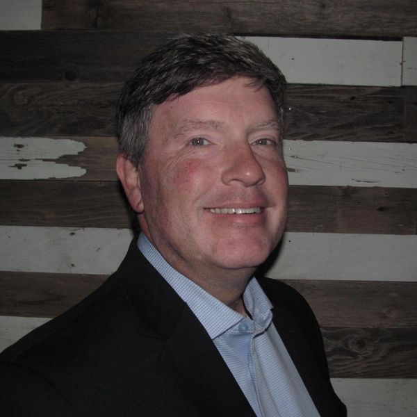 Man in suit smiling against a wooden background.