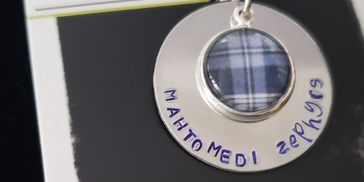 Silver pendant necklace with blue plaid center and handwritten text.