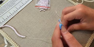 Hands beading bracelet string with small light pink beads.