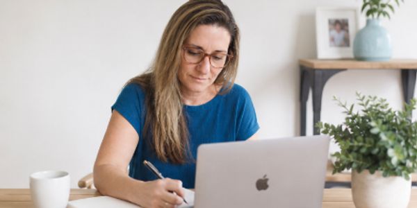 Woman working intently on a laptop and taking notes.
