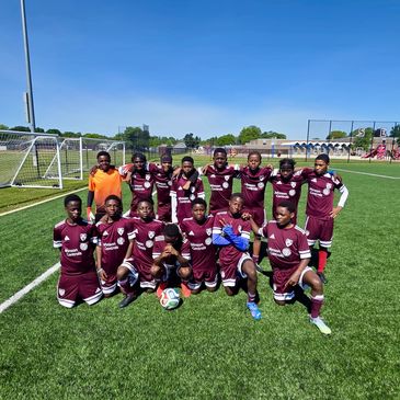 Youth soccer team in maroon uniforms posing on green field.