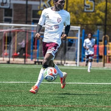 Soccer player in white and maroon uniform controlling the ball on the field.