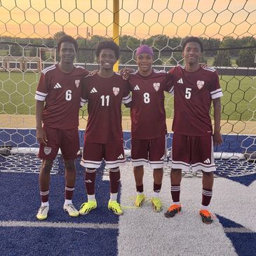 Four soccer players in maroon uniforms posing on a soccer field.