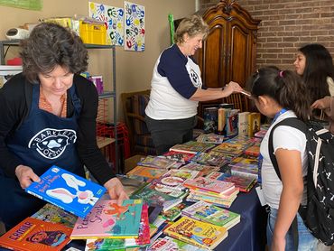 Two women organizing books for children at a table.