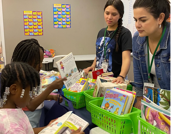 Children exploring books with two adults in a classroom.