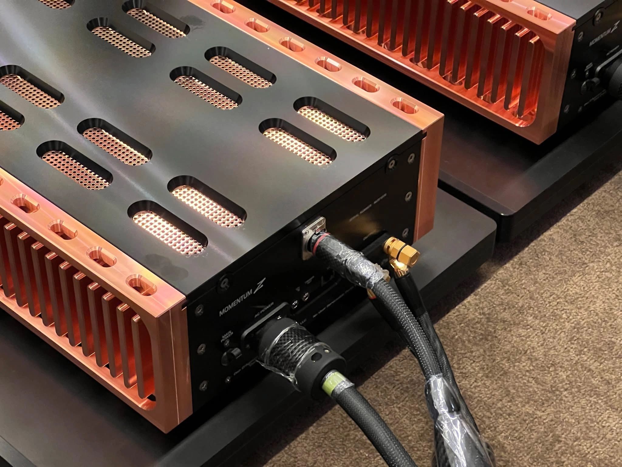 Close-up of high-end audio equipment with copper heat sinks and thick cables.