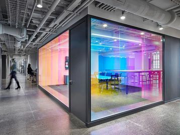 Modern open plan office with exposed ceiling, storage, and glass-partitioned meeting room. Vibrant d