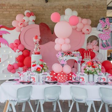 Pink and red Minnie Mouse themed birthday party setup with balloons and decorations.