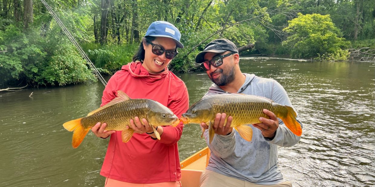 Two people holding fish and smiling on a river.