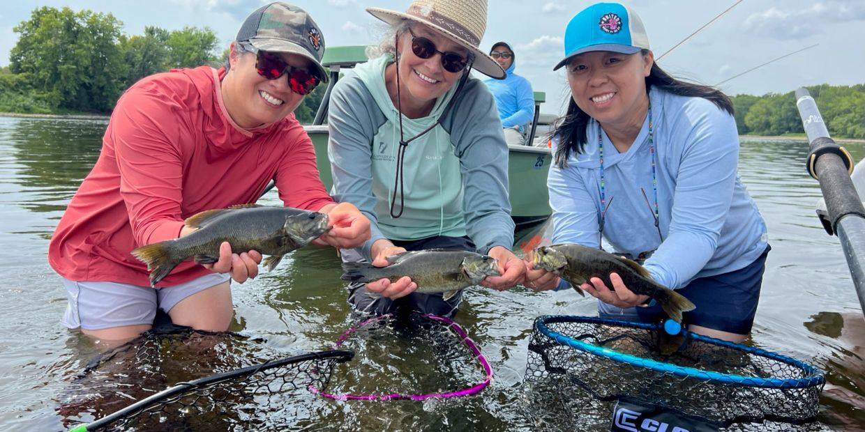 Three women holding fish by a river.