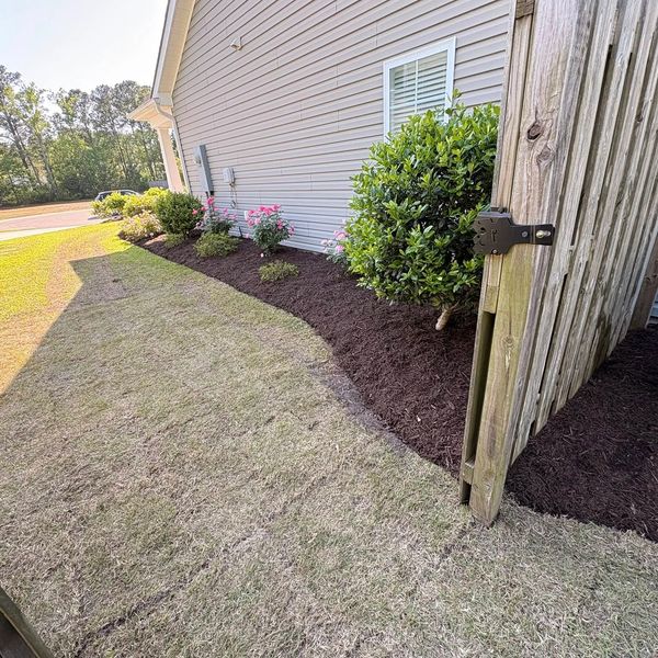 Freshly mulched flower bed along a house with a wooden gate open.